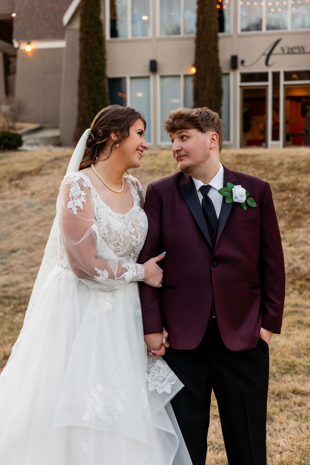 Bride and groom hold hands and smile at each other outside wedding venue.