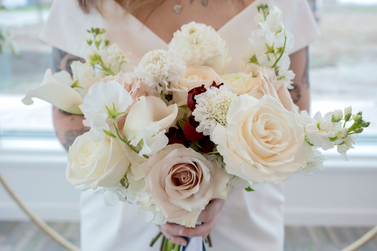 Photo of a bride holding a bouquet of flowers showing neutral colours with a pop of burgundy and blush.