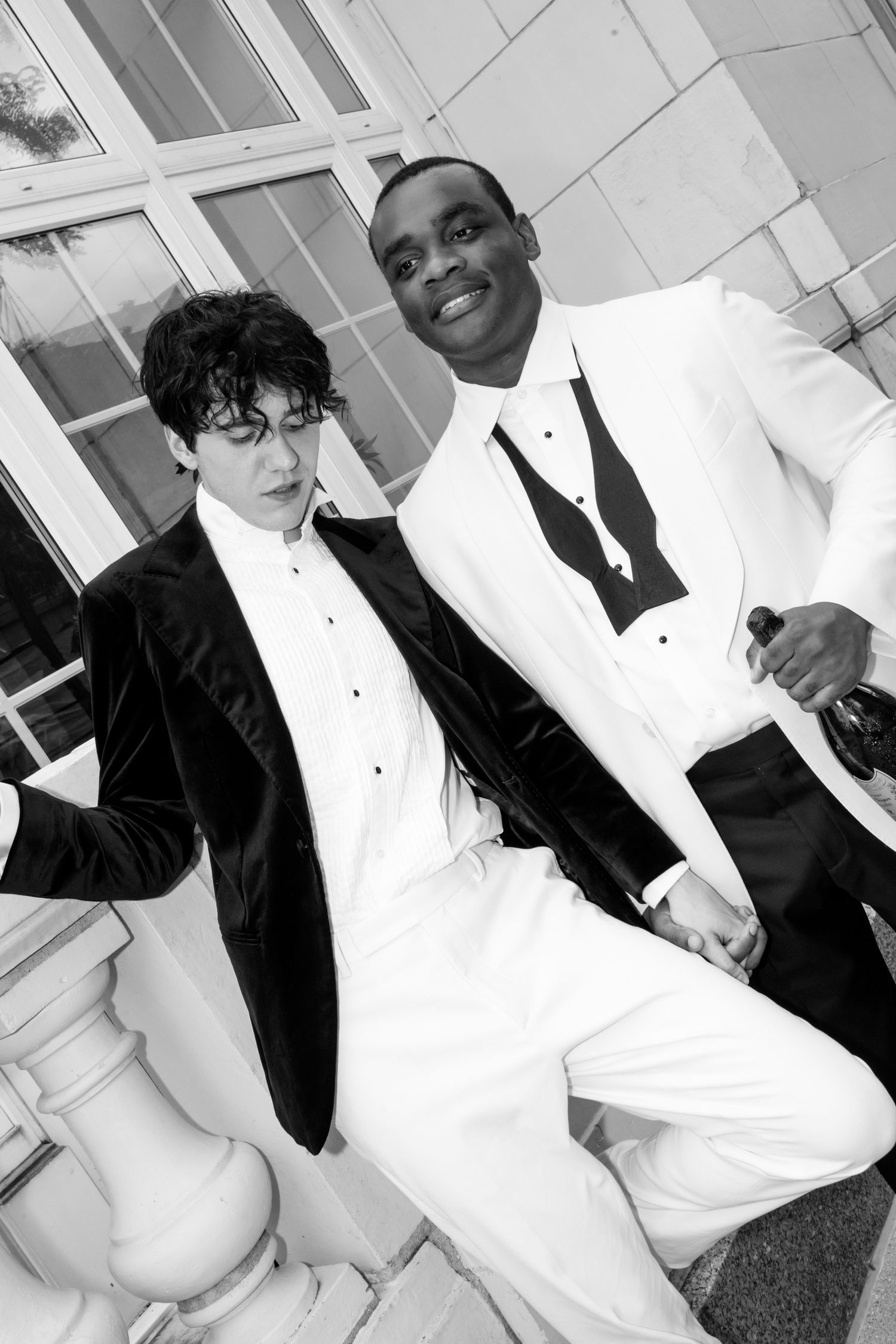Two men in formal tuxedos, one black and one white suit, posing together in a black and white photo.