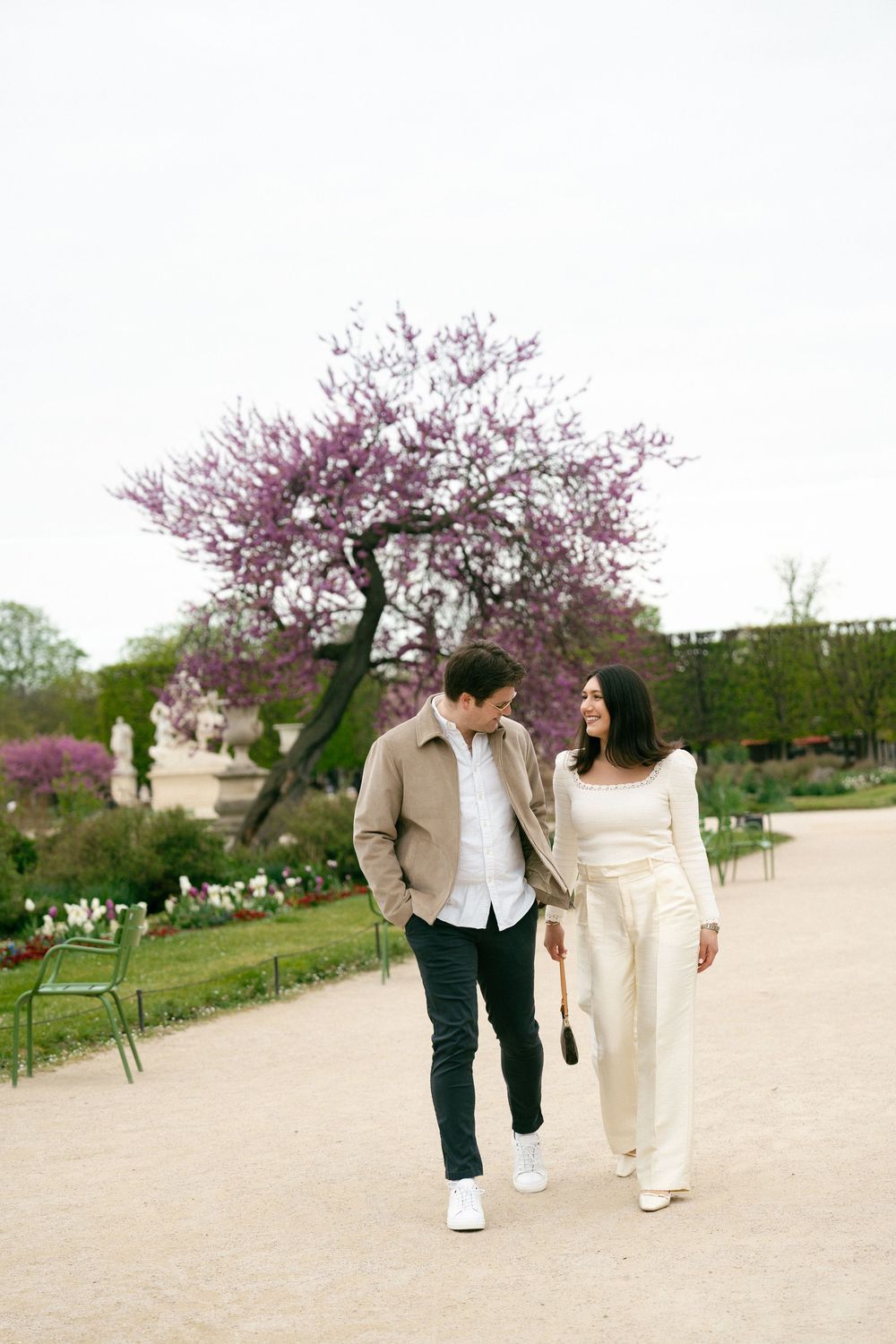 Couple walking hand in hand through a garden path with blooming cherry blossom trees in spring. Paris tuileries gardens photoshoot, Paris