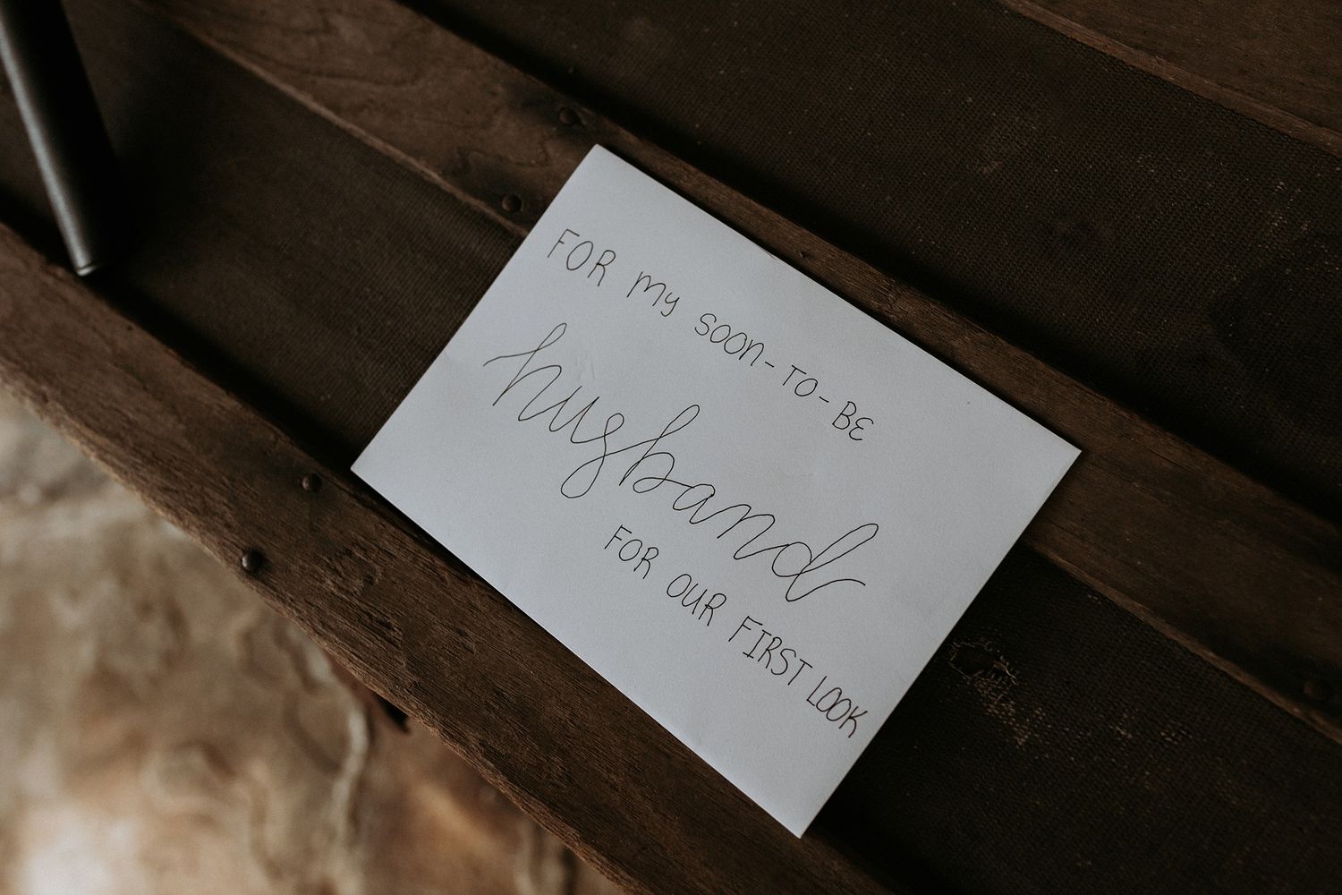 Handwritten note on white card reading 'For my soon-to-be husband, for our first look' placed on wooden surface.