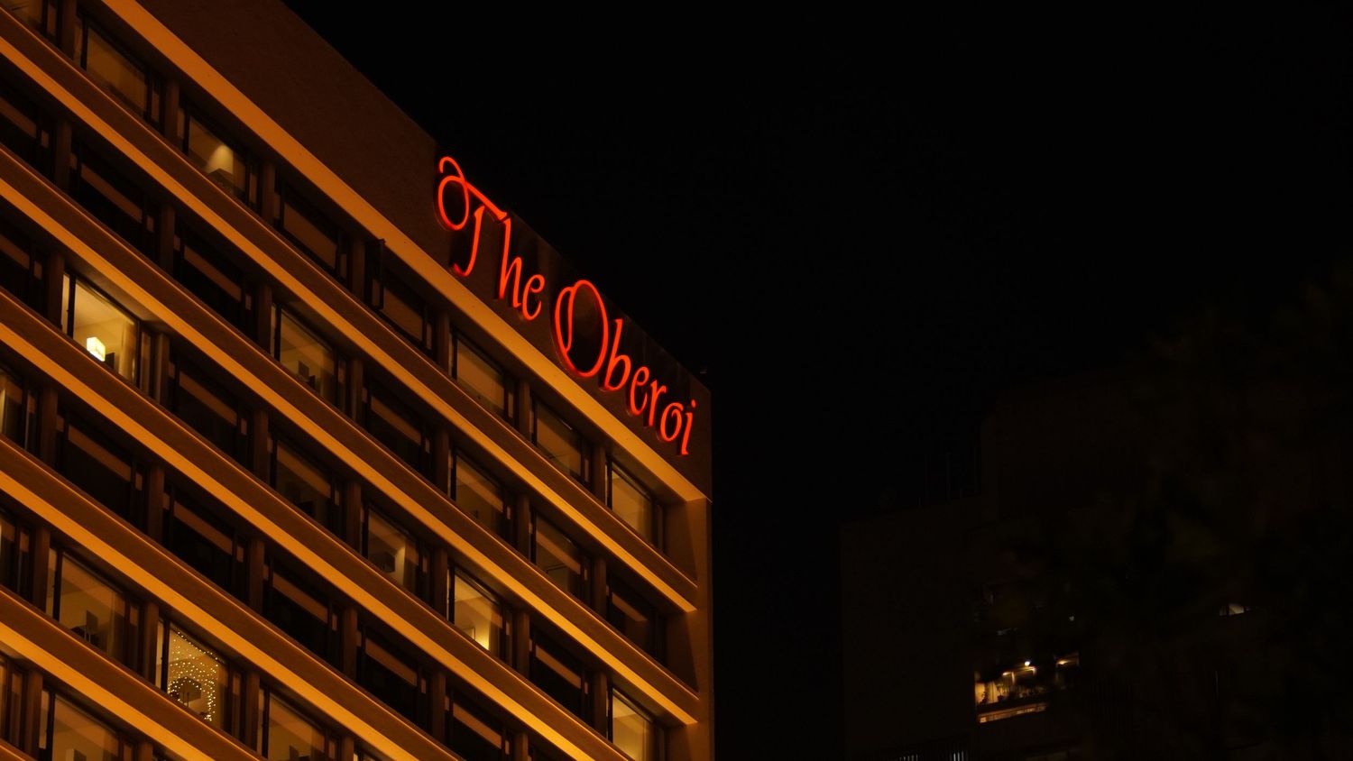 Dramatic night photography of a luxury building façade with red neon signage, highlighting urban geometry and light.