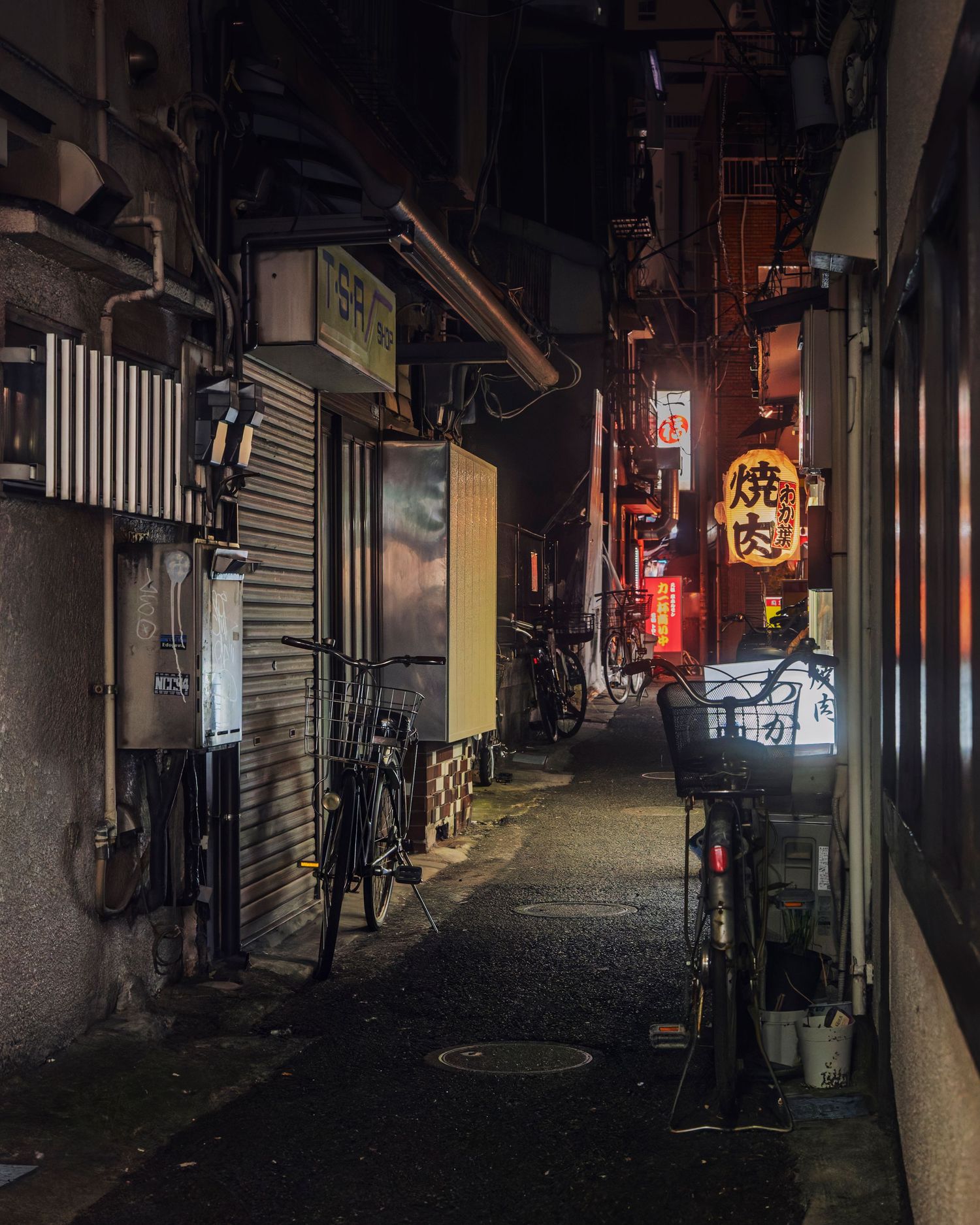 Narrow Japanese alleyway at night with glowing yakiniku restaurant sign and parked bicycles in moody urban setting.