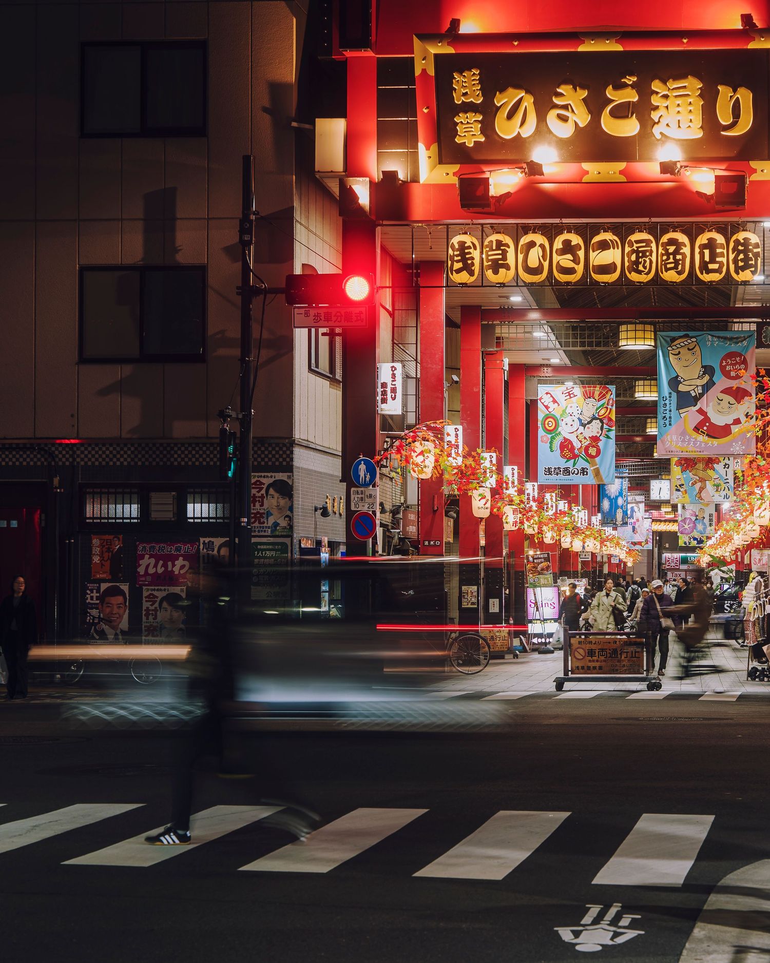 Vibrant Japanese shopping street at night with red lanterns, neon signs, and blurred motion near a crosswalk.