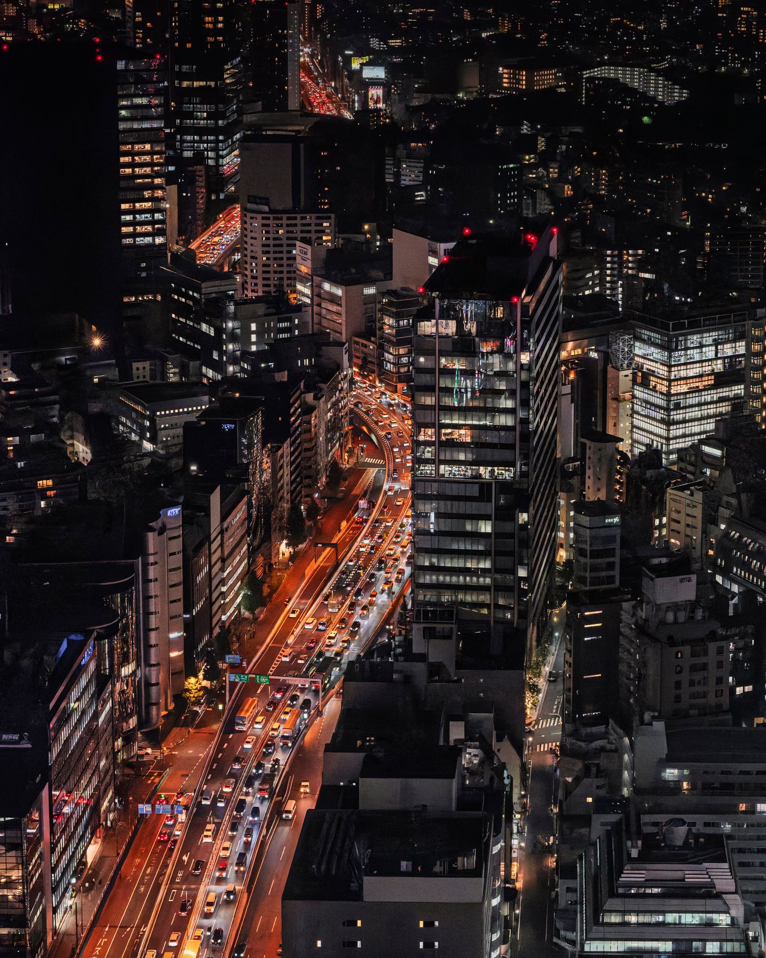 Aerial night view of a busy city street with glowing red traffic lights and illuminated skyscrapers.
