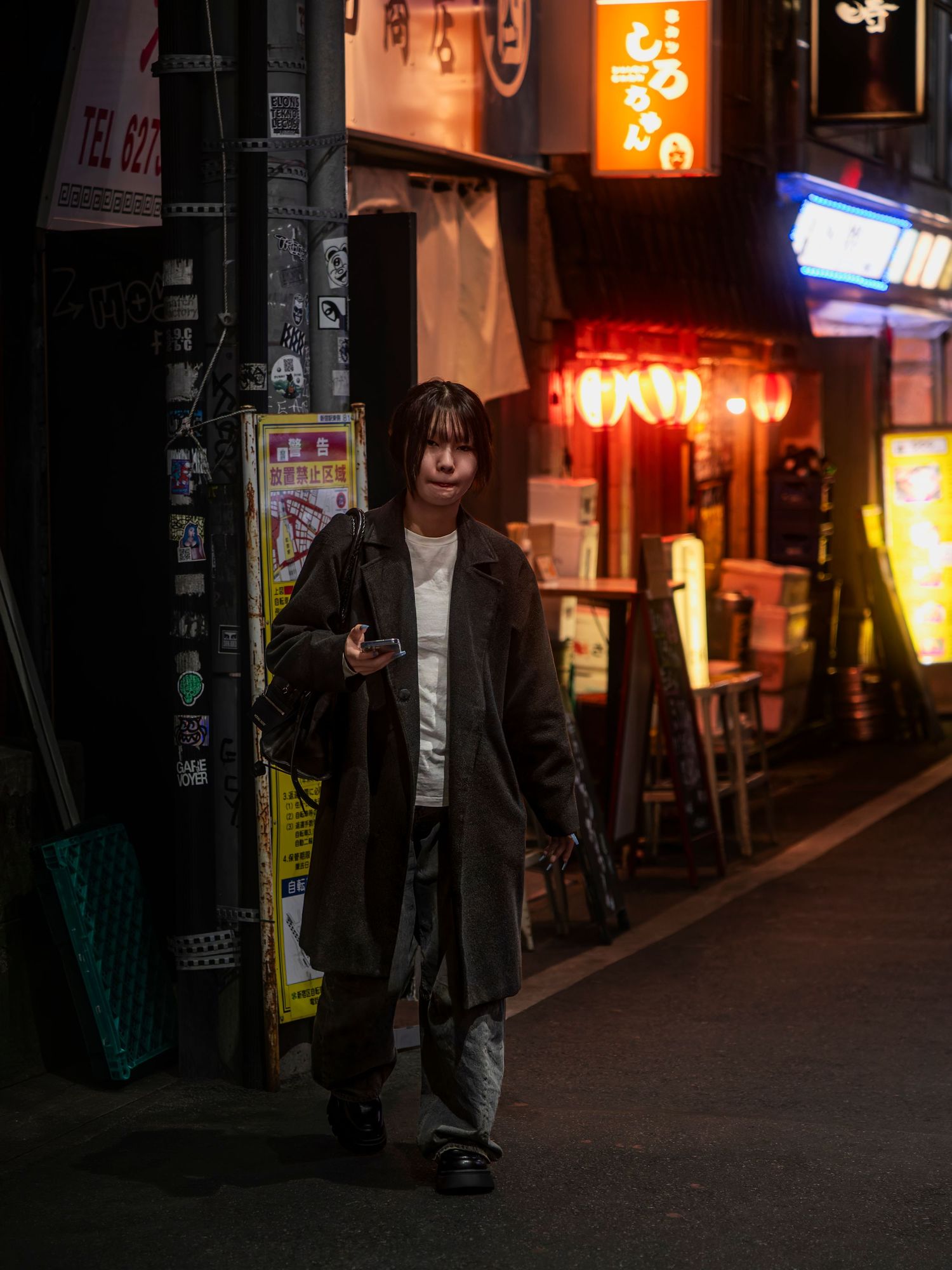 Person walking at night on a neon-lit Japanese alley street wearing a dark coat.