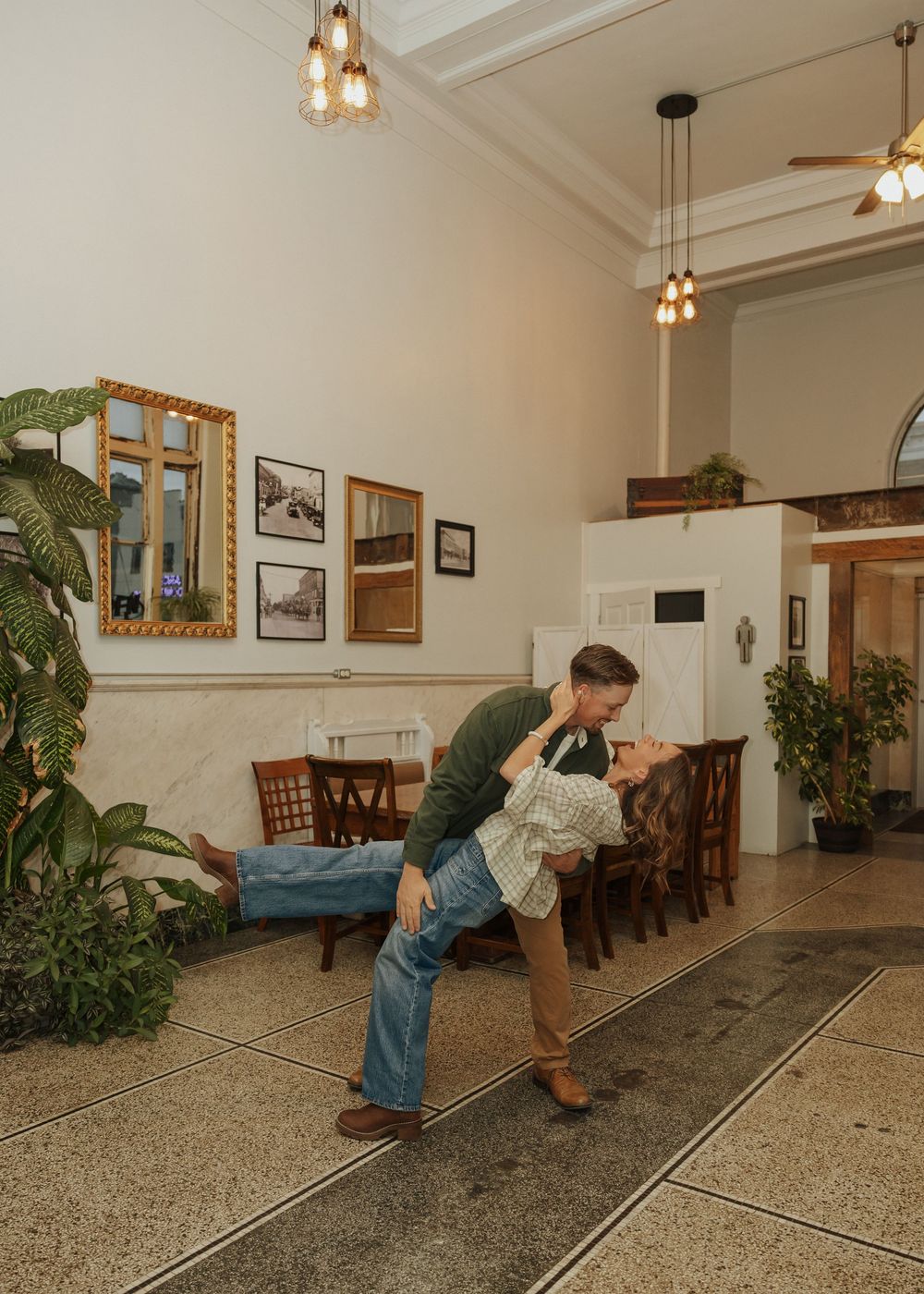 A couple shares a romantic dip kiss inside a warmly lit vintage hotel lobby with high ceilings.