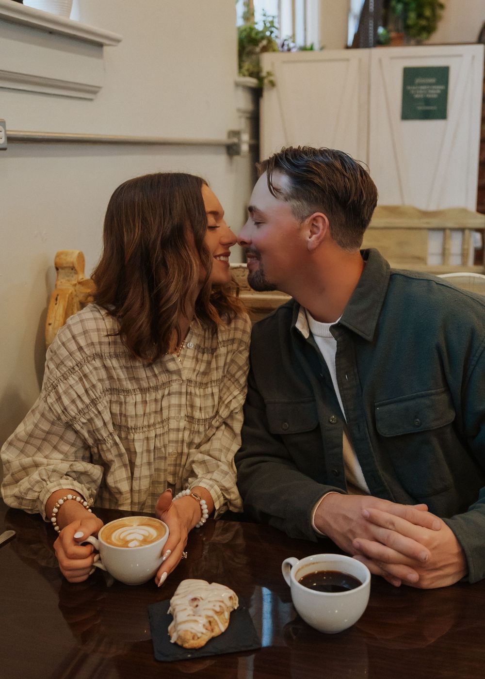 Couple sharing a romantic moment at a cafe table with lattes and pastries, smiling at each other.