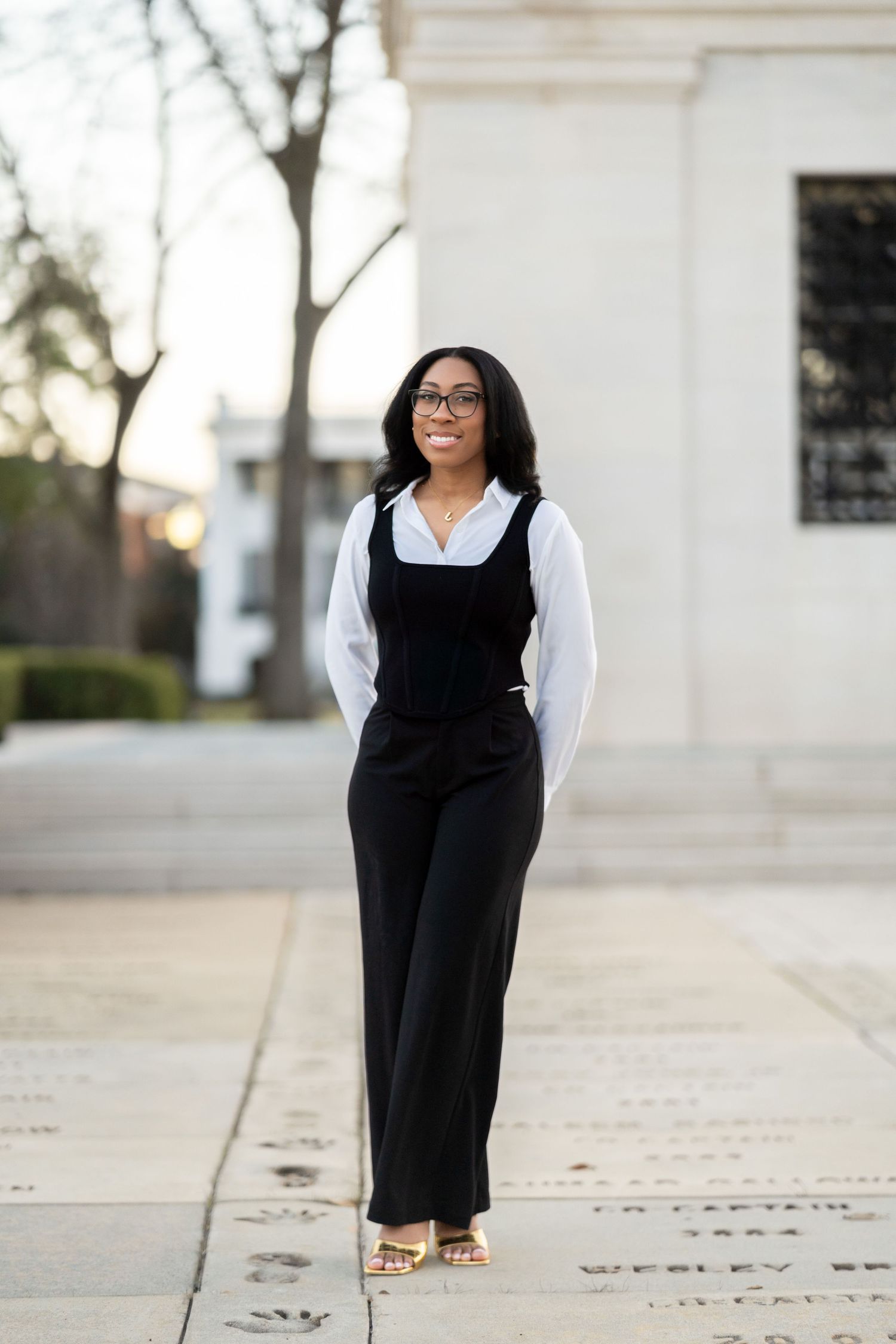 A person in a dark green button-down shirt and black velvet pants walks confidently down a walkway with a Gucci belt.