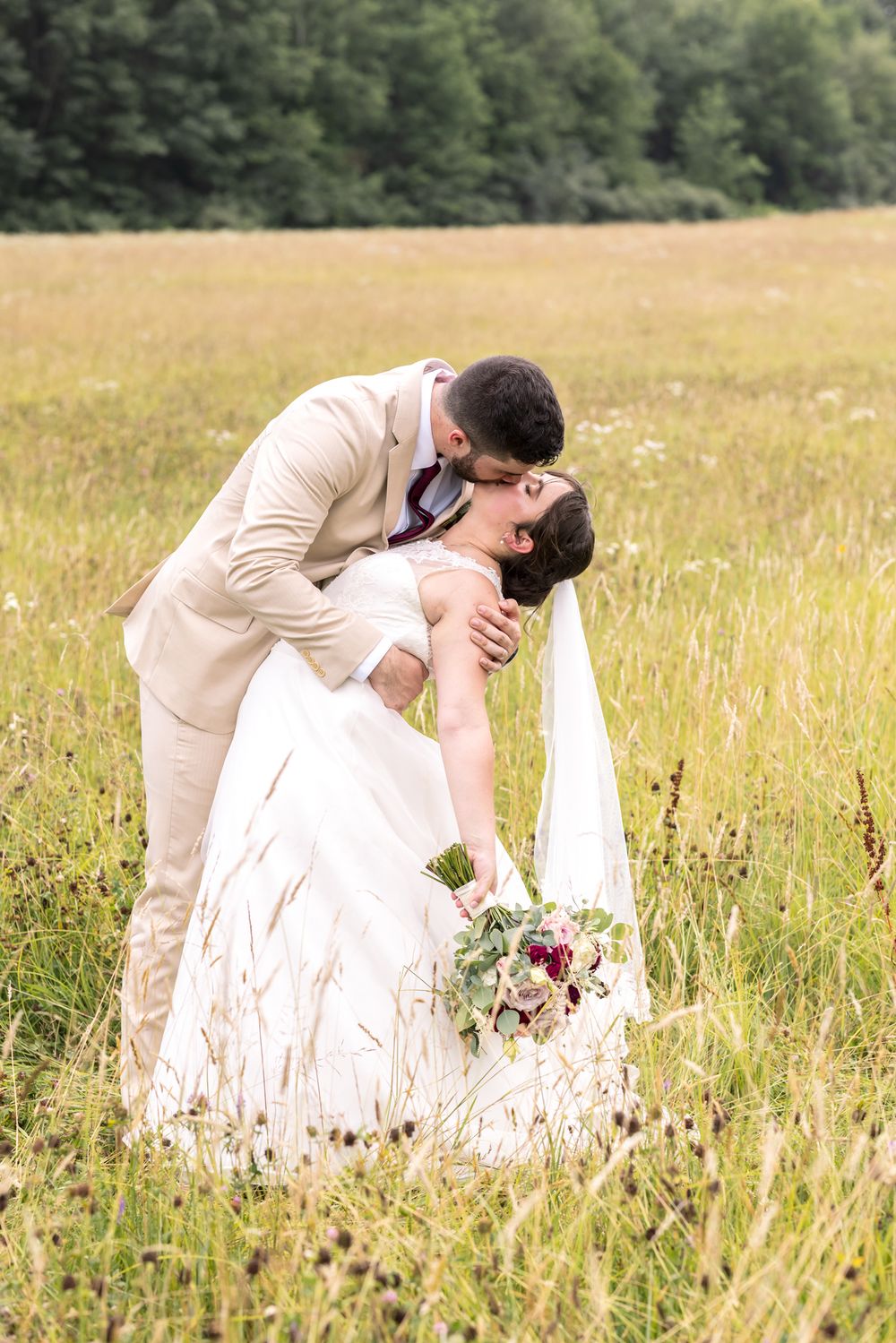 Groom bends bride for a dramatic kiss in a country field for wedding photos. Newburyport, Rochester, Dover wedding photographer