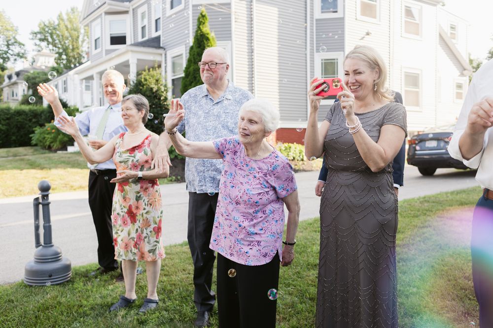 A grandmother waves goodbye with other wedding guests as bubbles blow about on a wedding day in Bradford, Essex County MA.