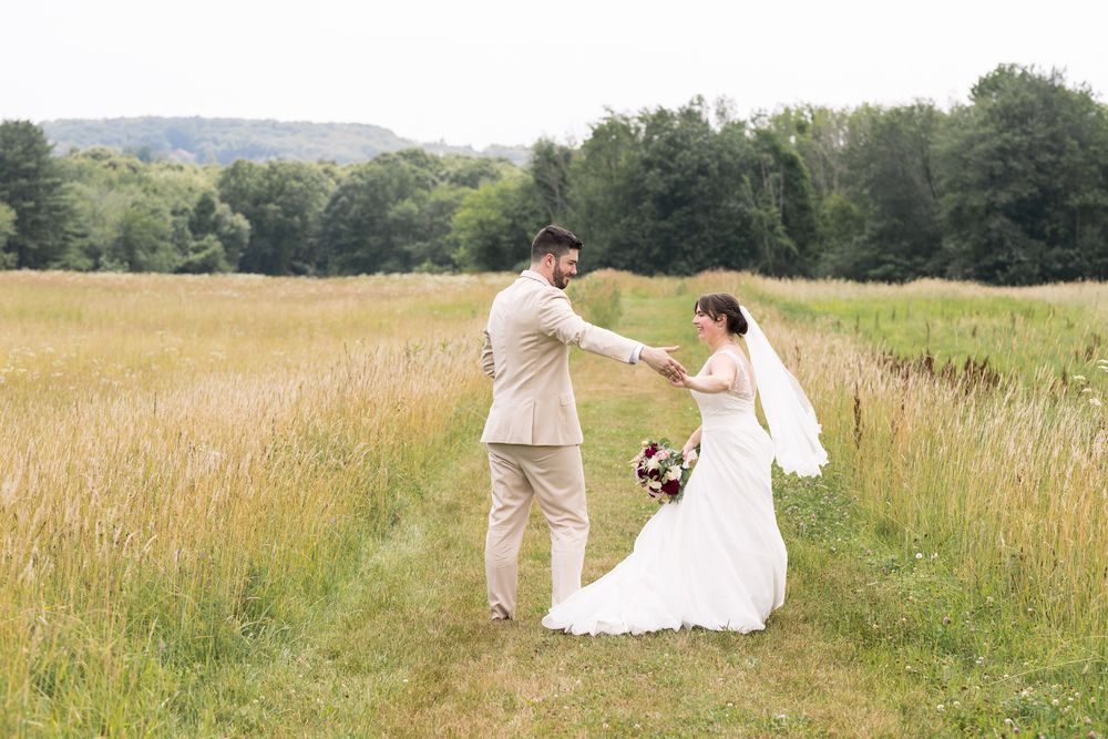 A groom spins his bride in a country field on a cloudy day for wedding photos. Concord, Bedford, Keene wedding photographer
