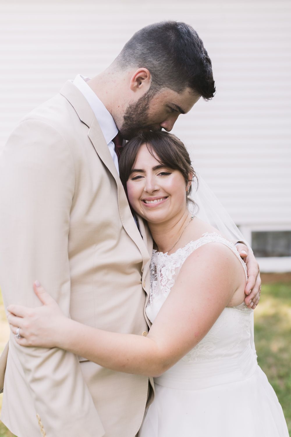 A happy, smiling bride is kissed on top of her head by her groom on their wedding day in Bradford, Essex MA. Hampton wedding photographer