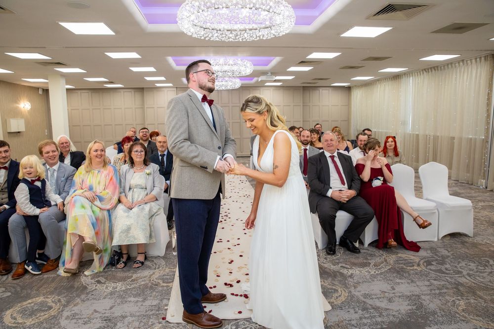 Bride and groom exchange vows during indoor wedding ceremony with seated guests in elegant chandelier ballroom.