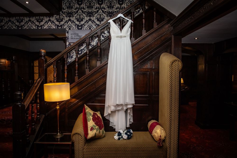 Elegant white wedding dress displayed on staircase in luxurious dark wood interior venue setting.