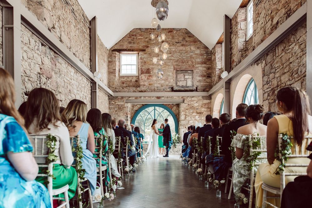 Wedding ceremony in a rustic stone chapel with guests seated in rows and a blue arched doorway at the end.