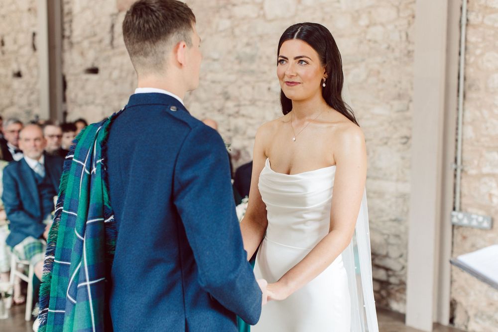 A couple in wedding attire stands in a rustic stone building during their special day.