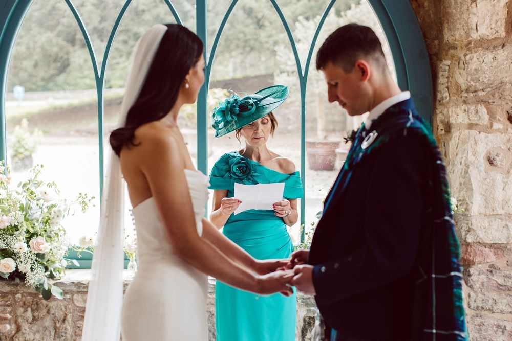 A couple in wedding attire exchanges rings during a romantic outdoor ceremony with turquoise accents.