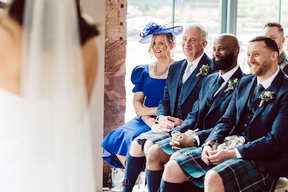 Wedding guests sit in rows and laugh during an outdoor ceremony at a rustic stone venue.