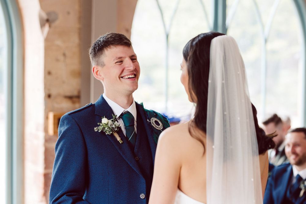 Bride and groom share a joyful moment during their wedding ceremony in a rustic brick venue.