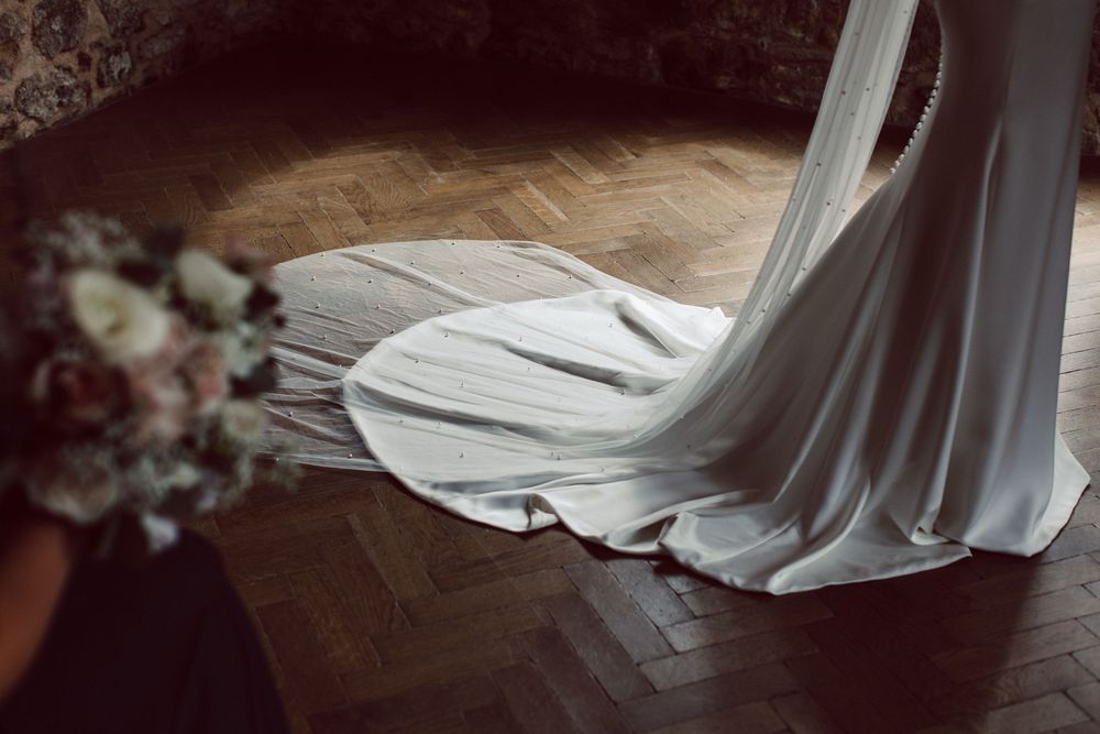 A flowing white wedding dress train draped elegantly across dark hardwood flooring.