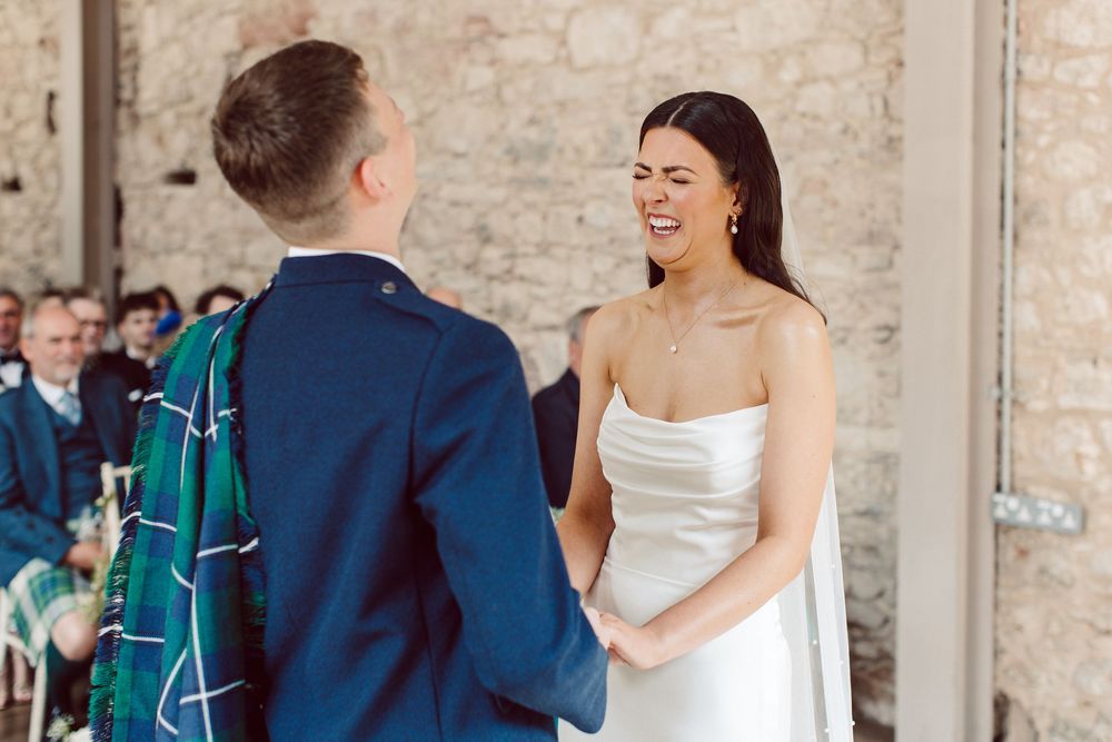 A joyful wedding celebration with the couple and guests sharing laughter outside a stone building.