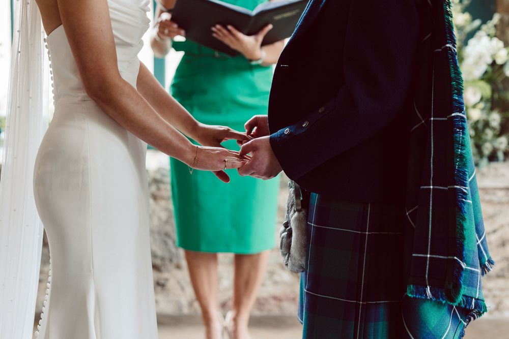A wedding party poses in a line wearing emerald green dresses and black suits in an outdoor garden setting.