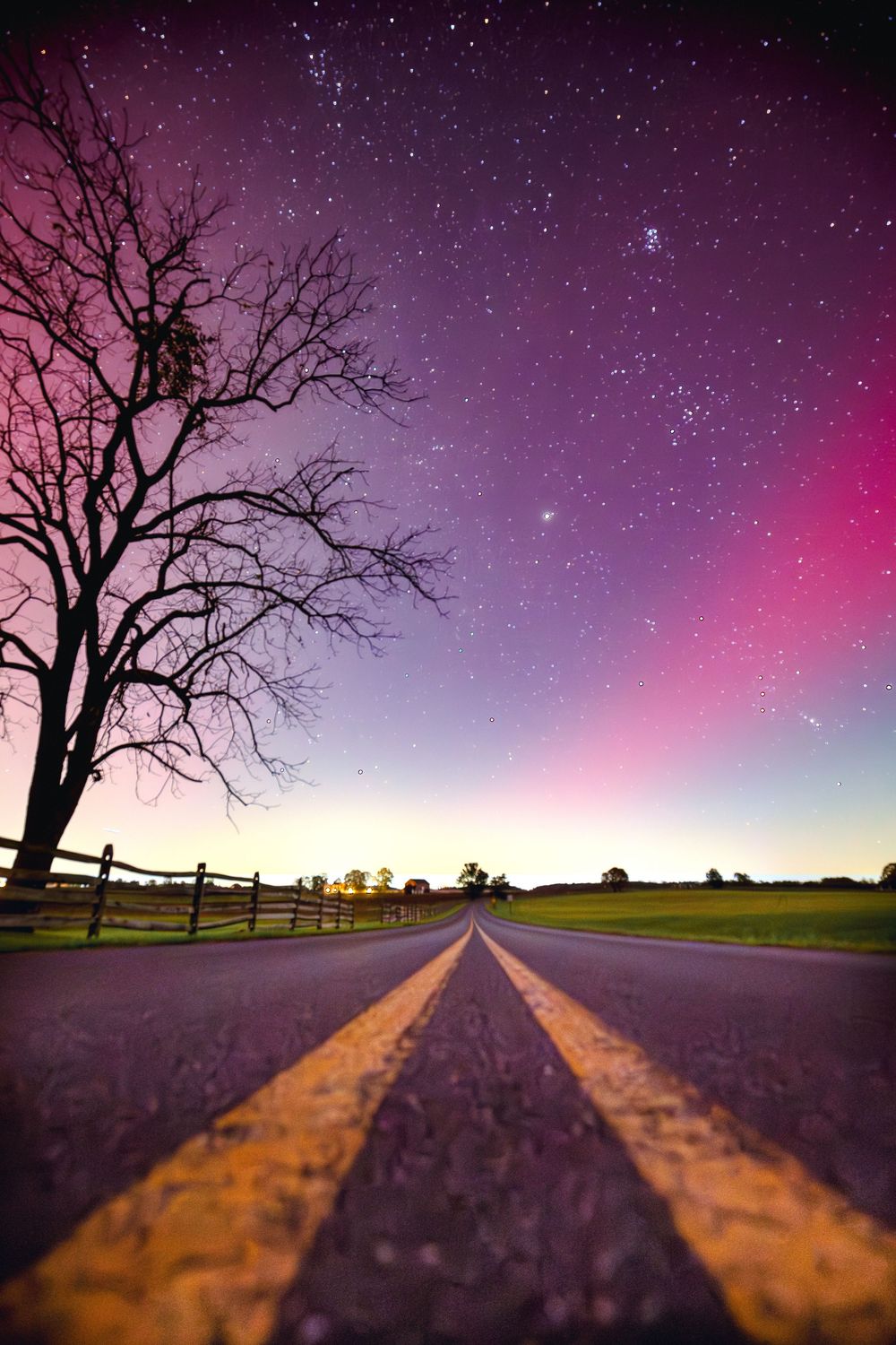Road with yellow lines stretches toward horizon under dramatic purple aurora borealis sky.