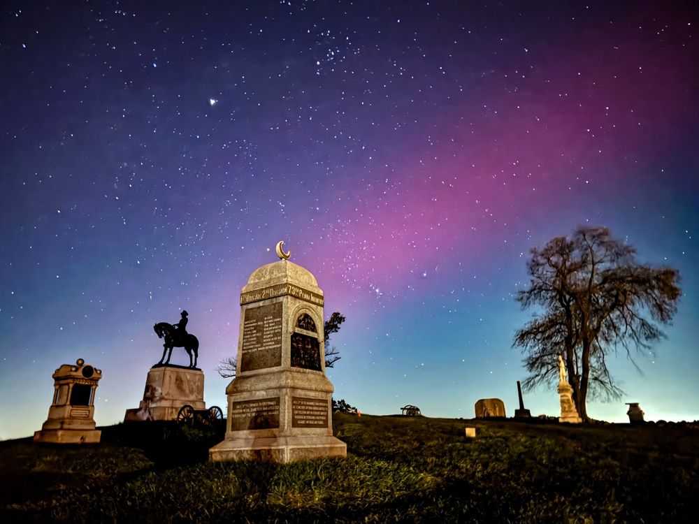 Silhouettes of buildings and trees against a vibrant purple and pink aurora borealis in the night sky.