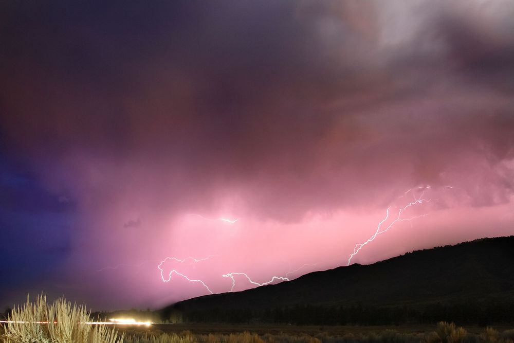 Lightning strikes illuminate pink and purple clouds during a dramatic sunset storm.