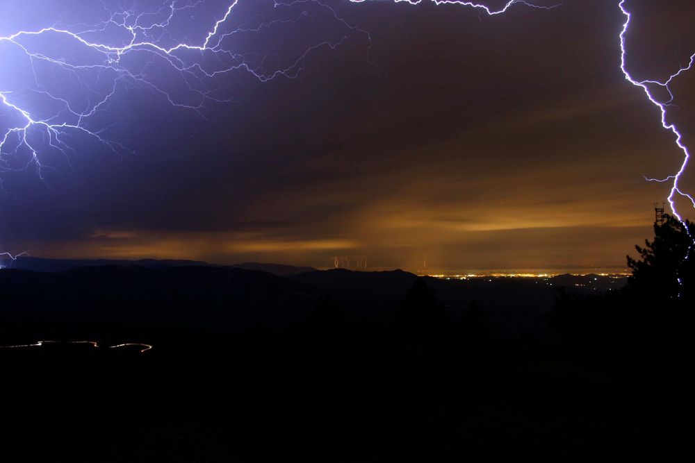 Multiple lightning bolts illuminate a dark stormy sky over a rural landscape at night.