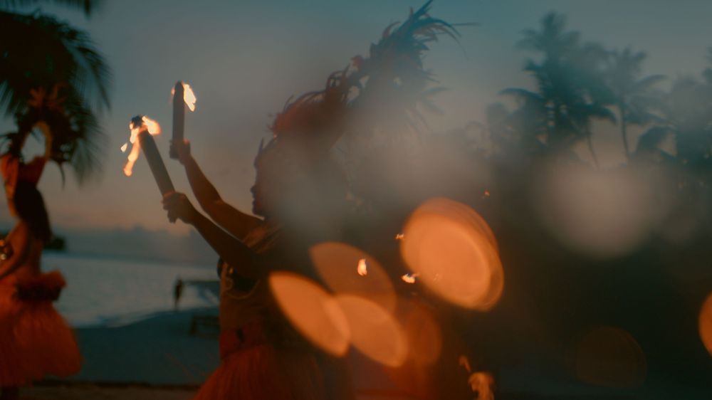 Palm trees silhouetted against a moody twilight sky with glowing orange bokeh lights creating a dreamy atmosphere.