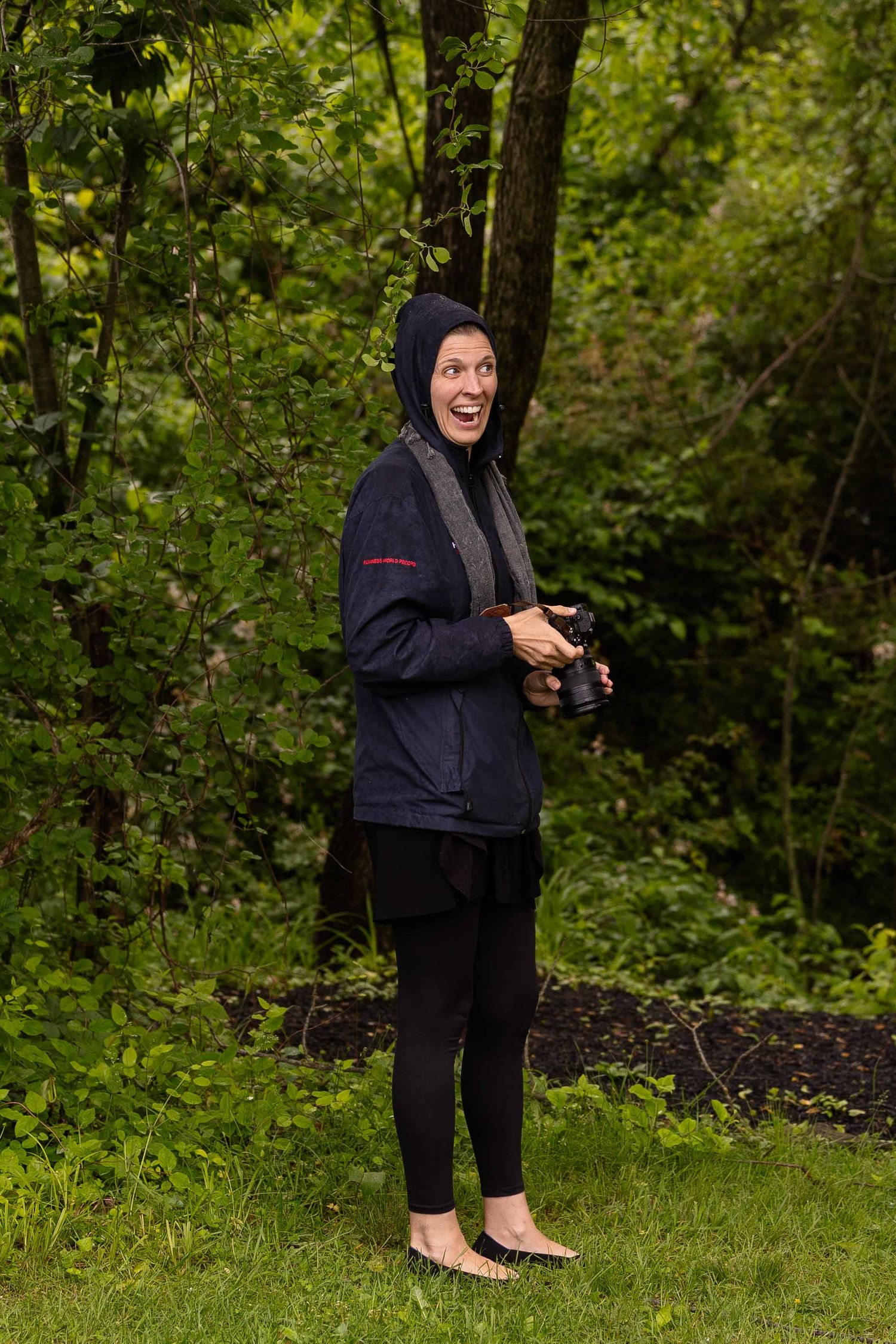 Someone in dark clothing stands in a lush green forest setting while holding a mobile device.
