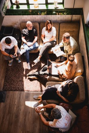 Group of people sitting on a couch looking at documents or papers together in a casual indoor setting.