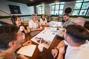 Business team collaborating around wooden table in modern office space with large windows.