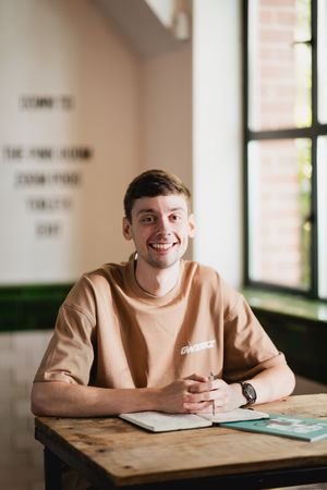 Student sitting at desk in classroom with natural lighting from windows and beige sweater.