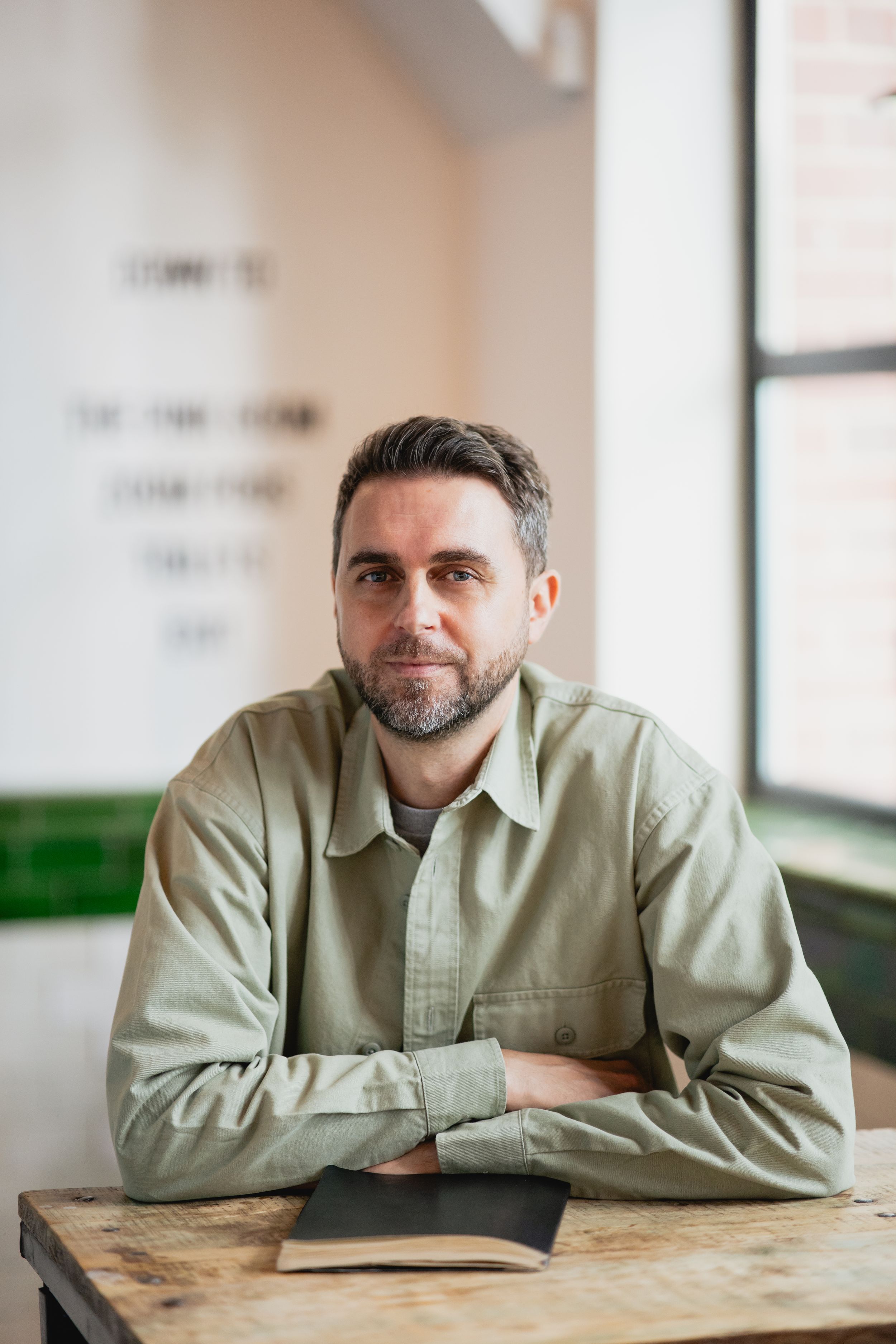 Person in light green jacket leaning on wooden table in bright interior space.