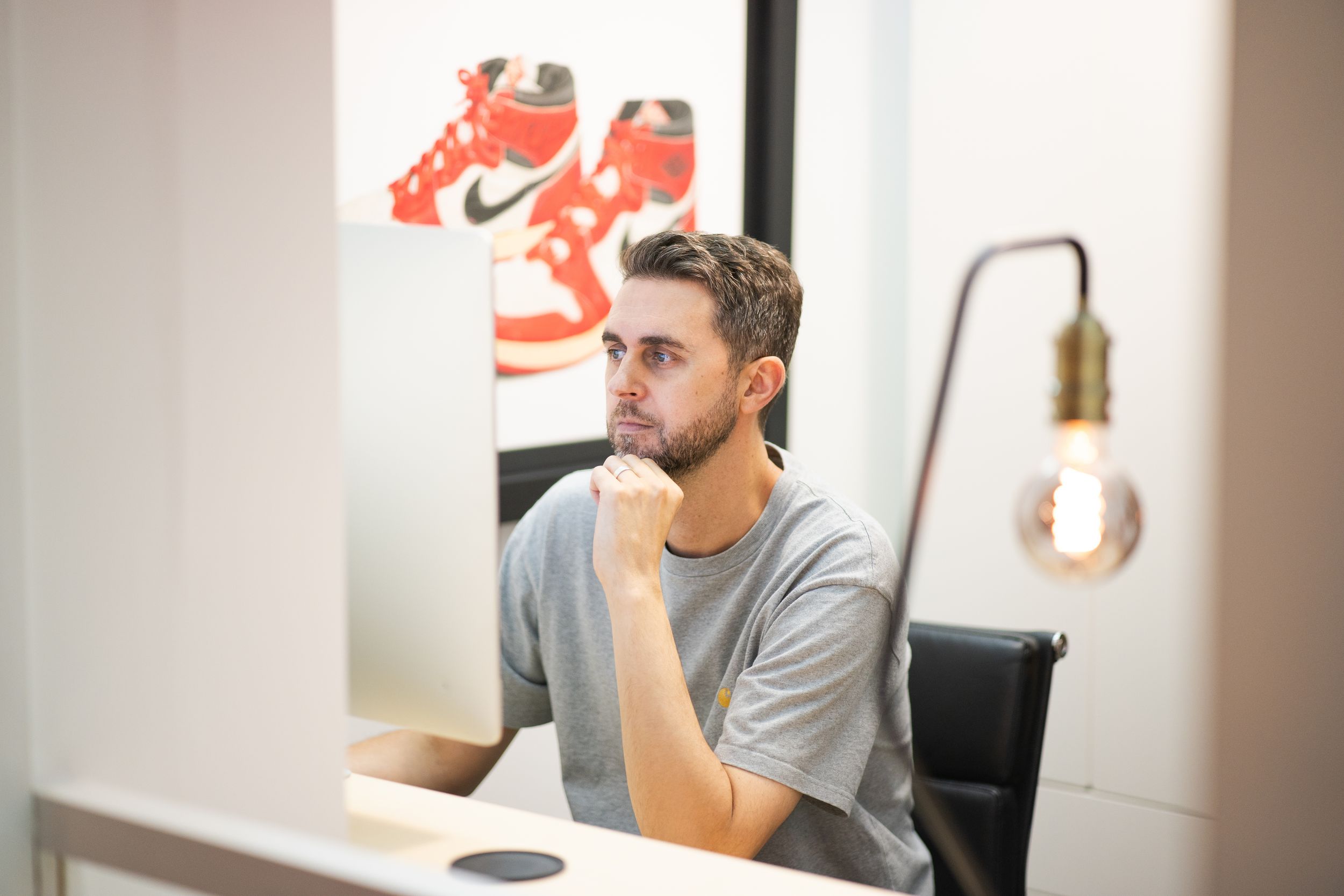 A person in a gray t-shirt sits at a desk in front of a laptop computer in a modern office setting.