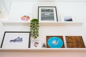 Modern office shelving displaying framed artwork and decorative plants against white wall.