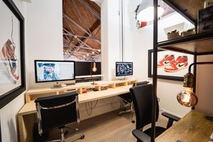 Industrial-style workspace with exposed ceiling, track lighting, and shelving units arranged along white walls.