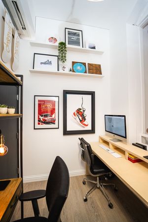 Modern office workspace with wooden desk, black chairs, and framed artwork on white walls.