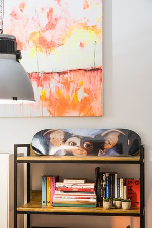 Modern living room shelf with books and decor under a vibrant orange and pink abstract painting.