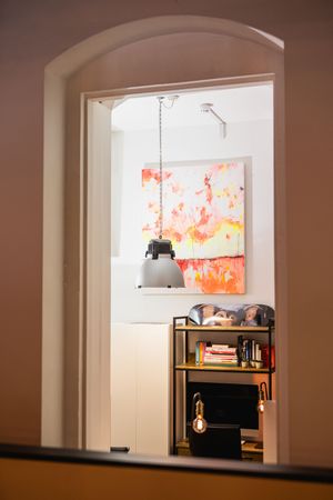 Sequence of arched doorways leading to a room with an illuminated orange and red art piece displayed in a window.