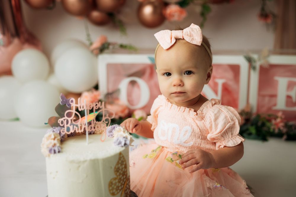 A pink and white themed birthday celebration setup with balloons, cake, and decorative elements.