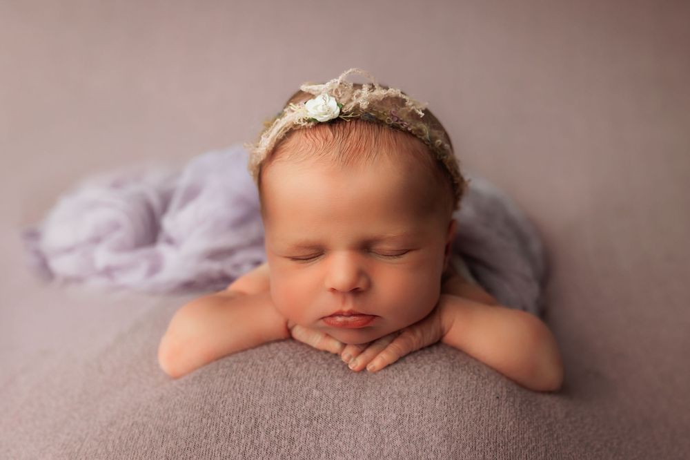 Sleeping newborn baby rests peacefully on soft pink blanket in professional portrait studio setting.