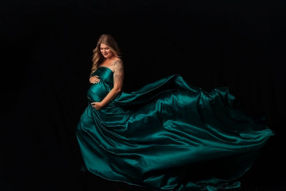 Flowing emerald green satin dress billows dramatically against dark background in fashion photography series.