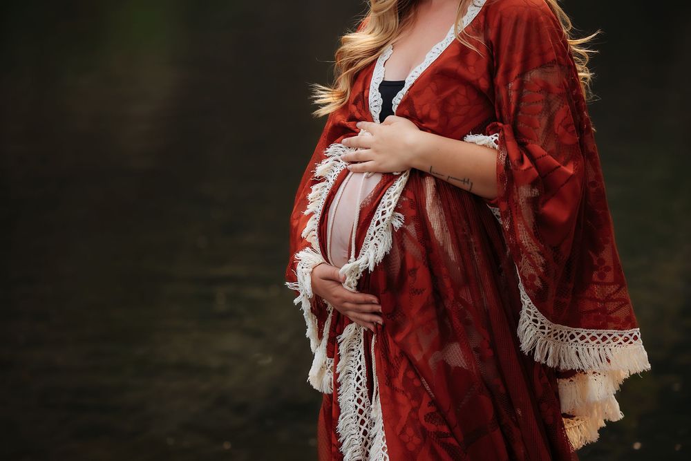 A figure in a flowing red velvet dress stands in a dreamy forest setting with soft natural lighting.