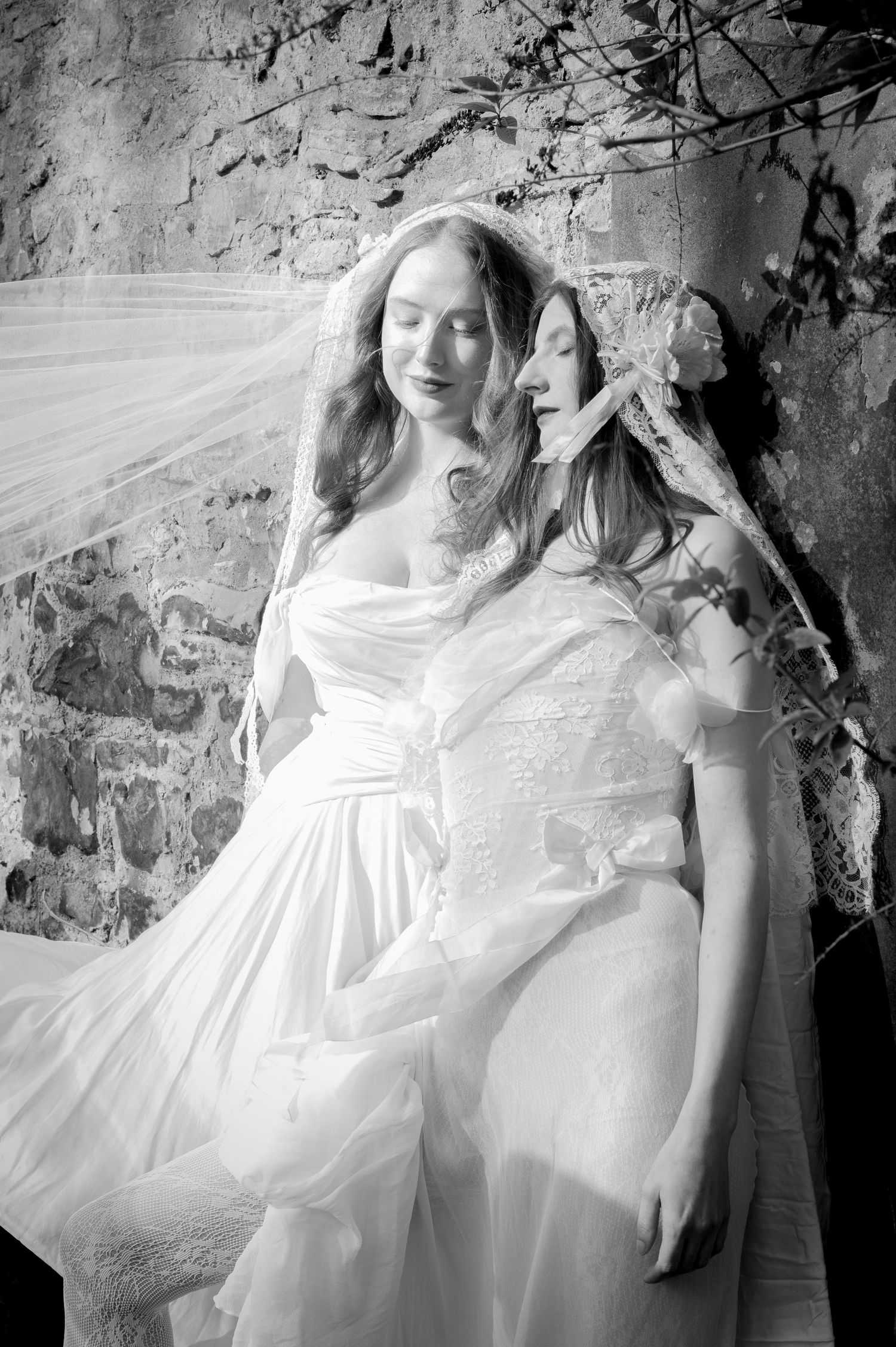 A series of black and white artistic photographs showing two figures in white dresses against a textured wall background.