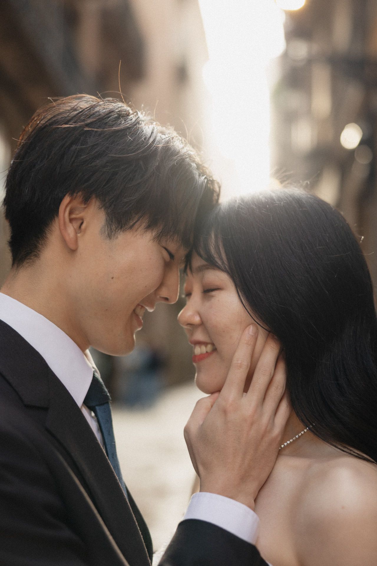 A romantic couple shares an intimate moment in formal attire as sunlight glows behind them.