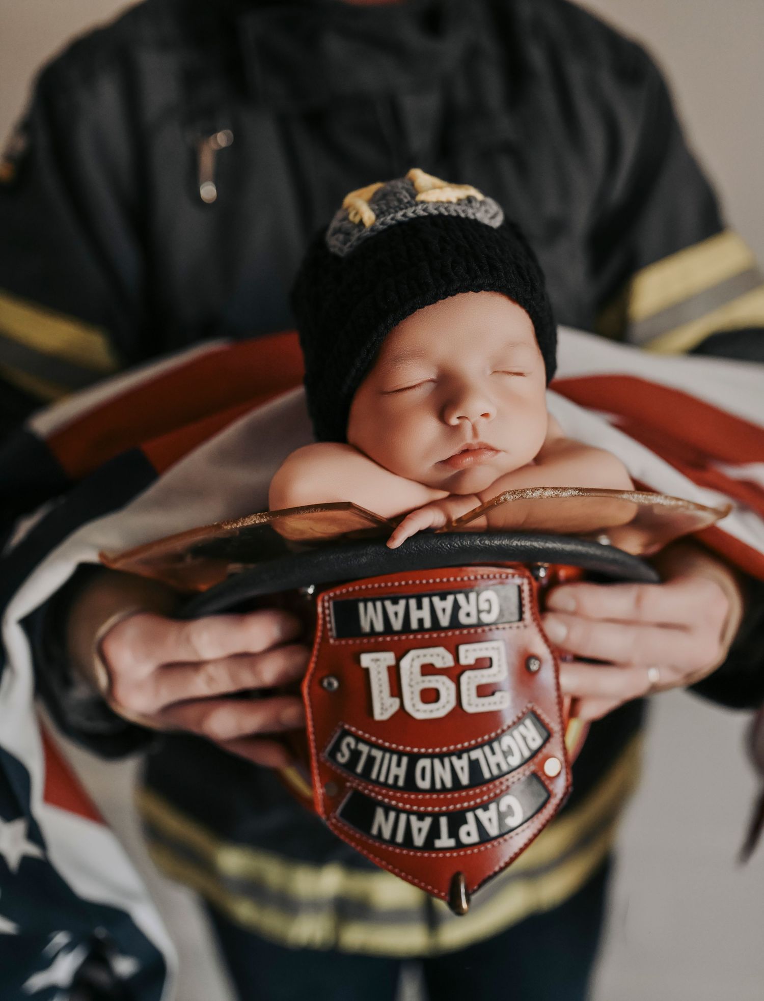 Father in firefighter role gently cradling newborn baby in a timeless studio portrait in Dallas Fort Worth